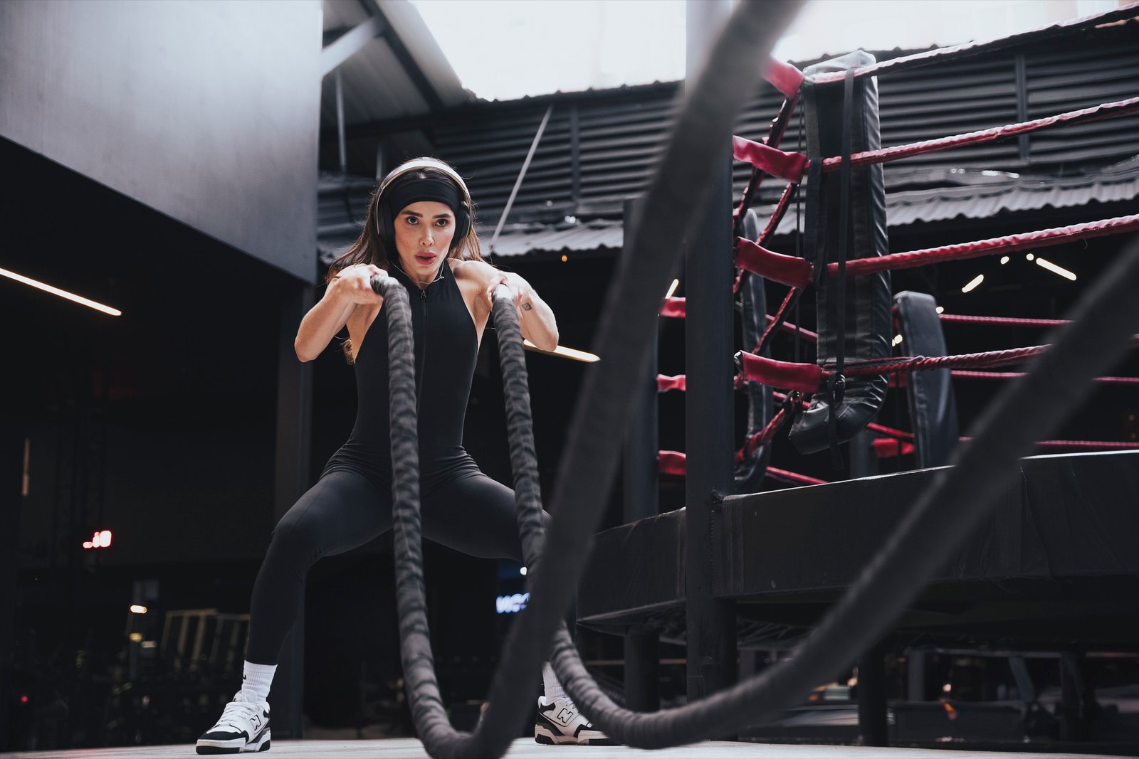 Mujer entrenando con cuerdas de batalla frente a un ring